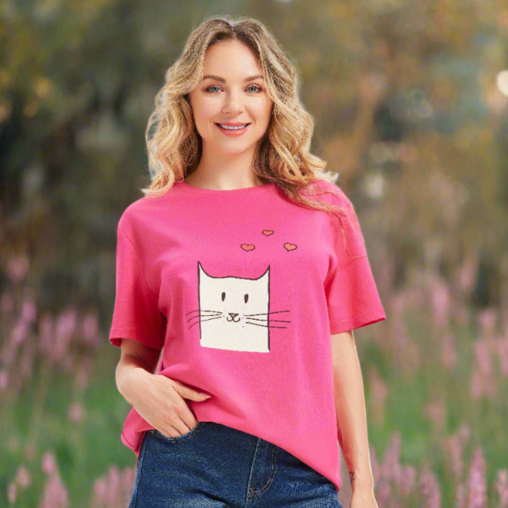 Woman wearing a pink t-shirt with a cat graphic and denim shorts on an outdoor background