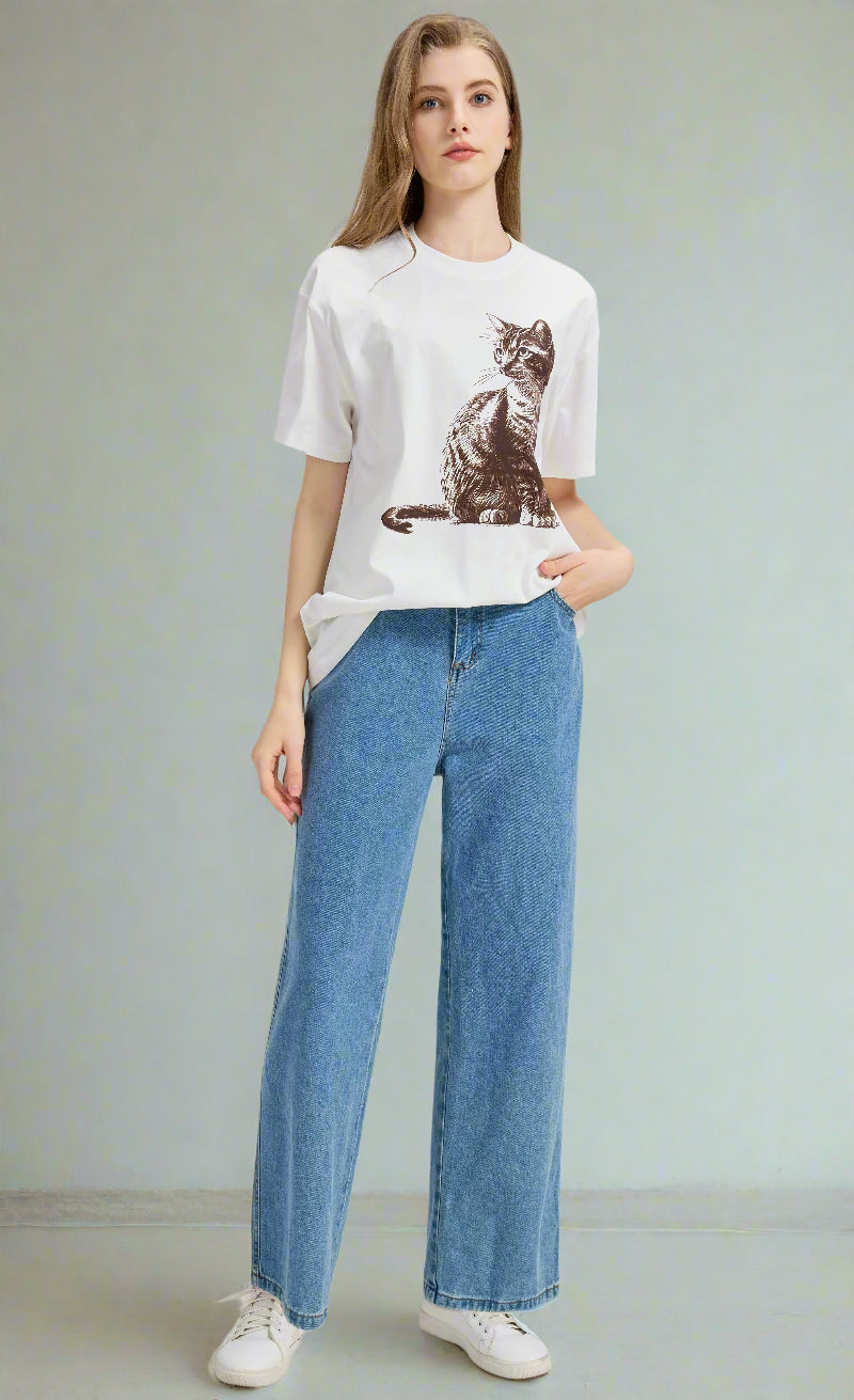 Woman wearing a white t-shirt with a cat graphic and blue jeans on a light gray background