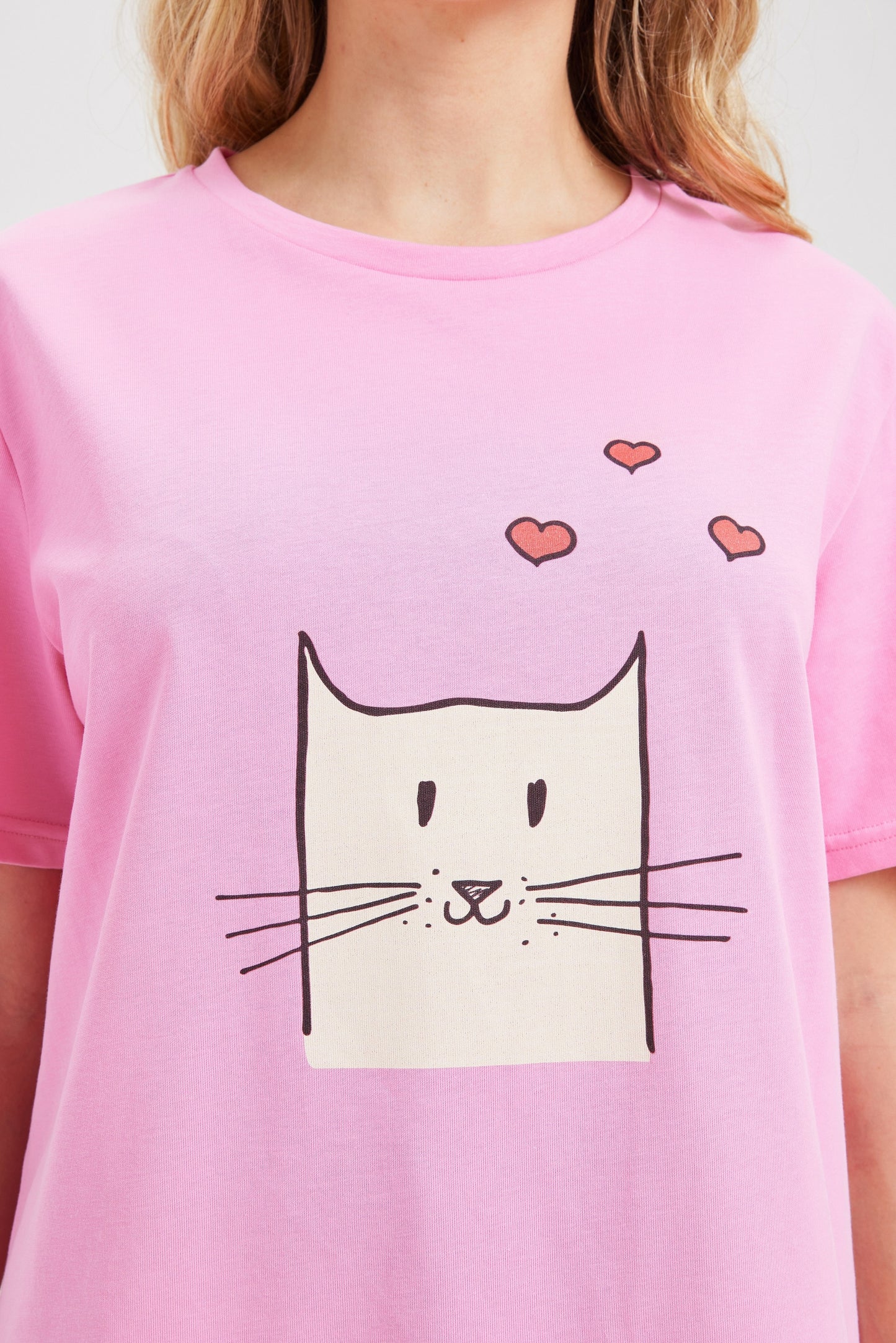 Pink t-shirt with a cat graphic and hearts on a white background